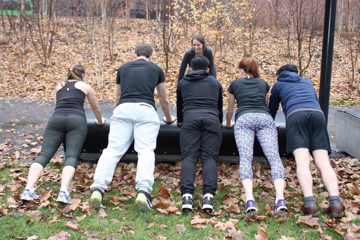 A personal trainer and five clients performing a press-up exercise on a park bench