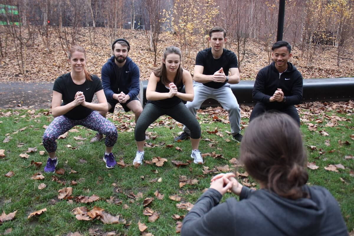 A personal trainer and five clients performing a squat exercise in a park